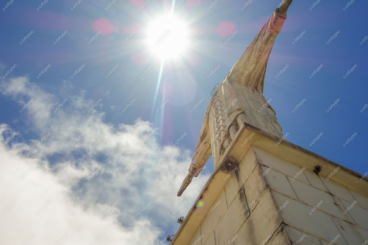 Cristo Redentor em Poços de Caldas sob luz intensa do sol com céu azul e montanhas ao fundo