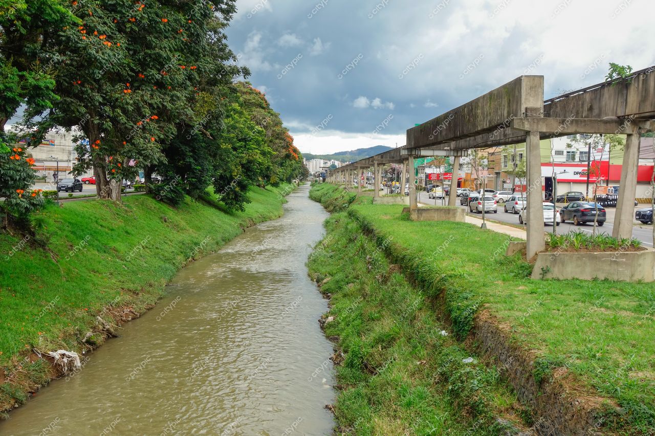 Centro de Poços de Caldas em Poços de Caldas com canal de água, vegetação verde e céu nublado com tráfego urbano