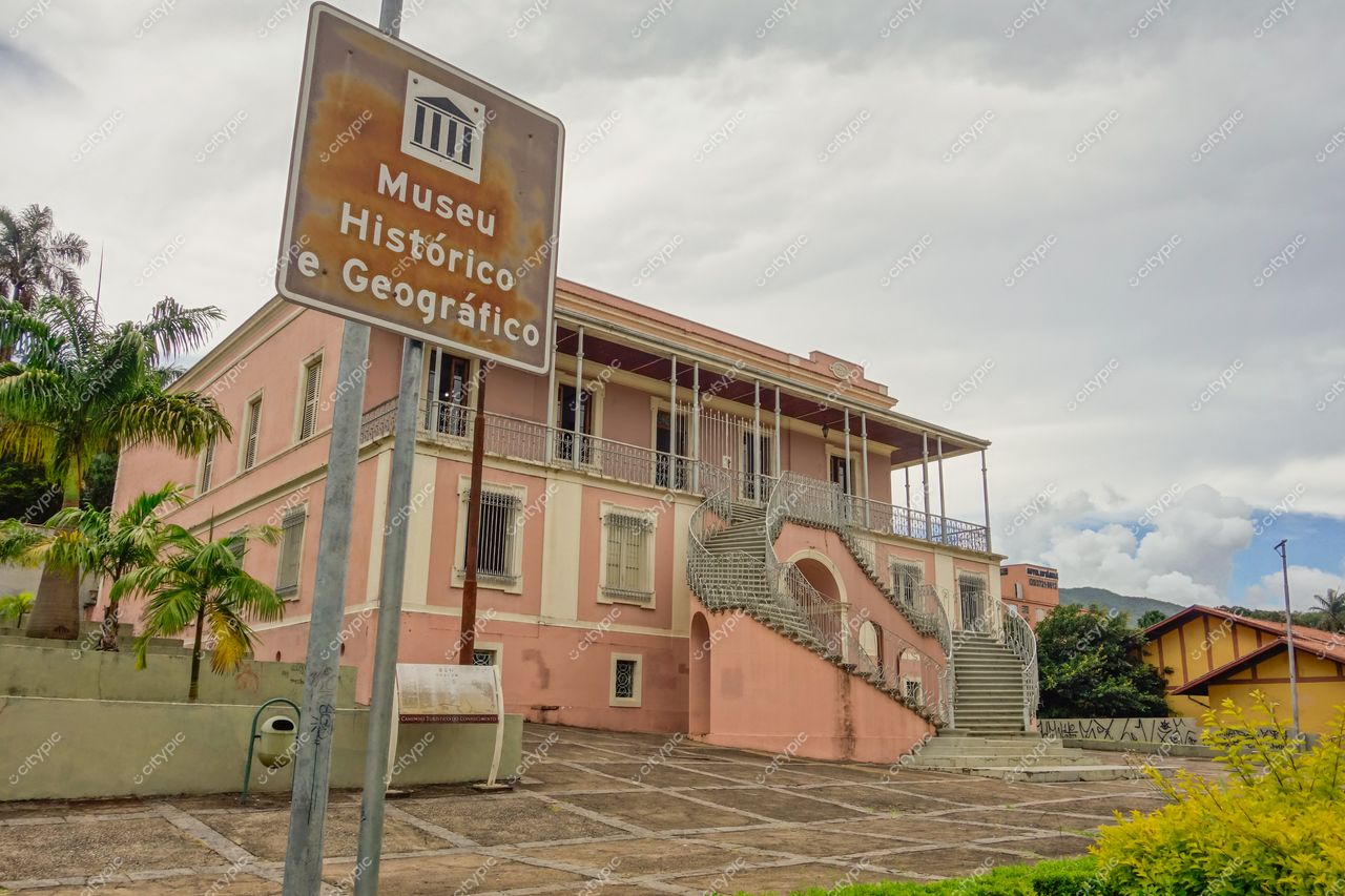 Museu Histórico e Geográfico de Poços de Caldas em dia nublado com vegetação tropical e placa informativa em primeiro plano