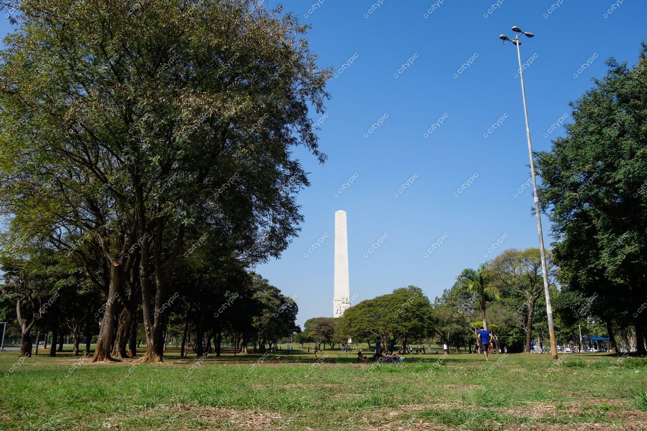 São Paulo, São Paulo, obelisco alto cercado por vegetação em dia ensolarado com céu azul e pessoas no parque
