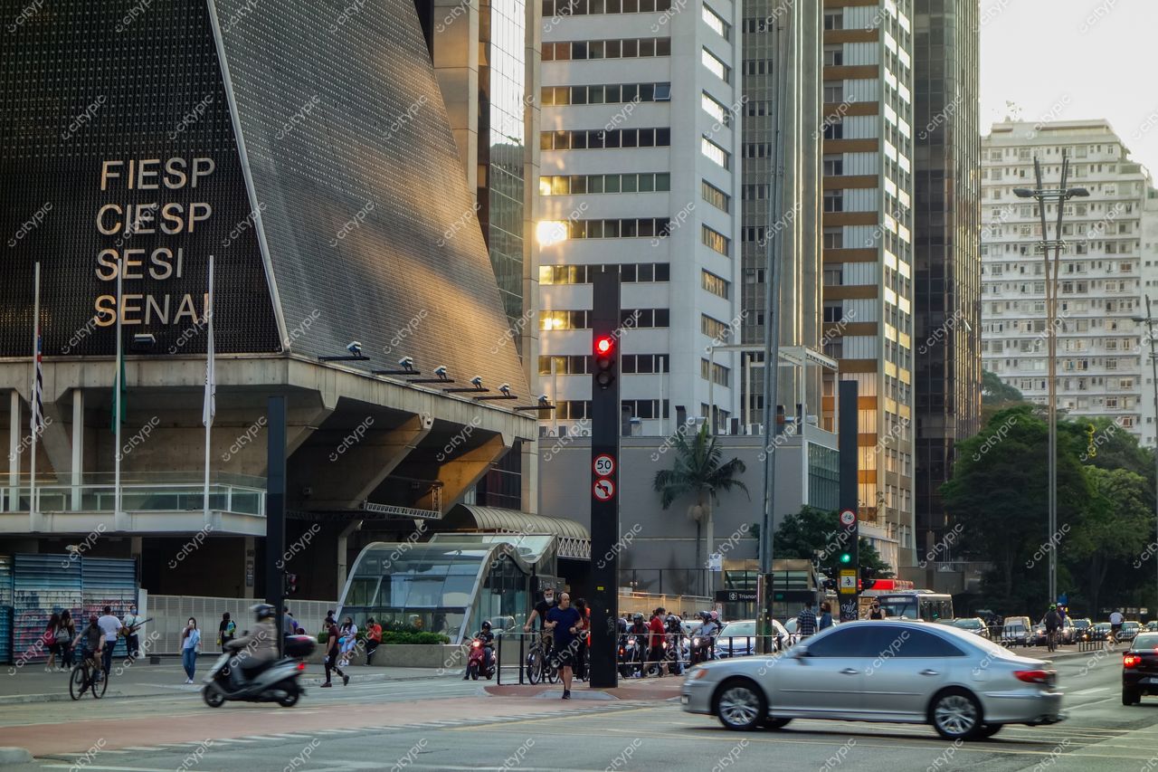 Avenida Paulista em São Paulo com edifício FIESP ao entardecer e movimento intenso de pedestres e veículos