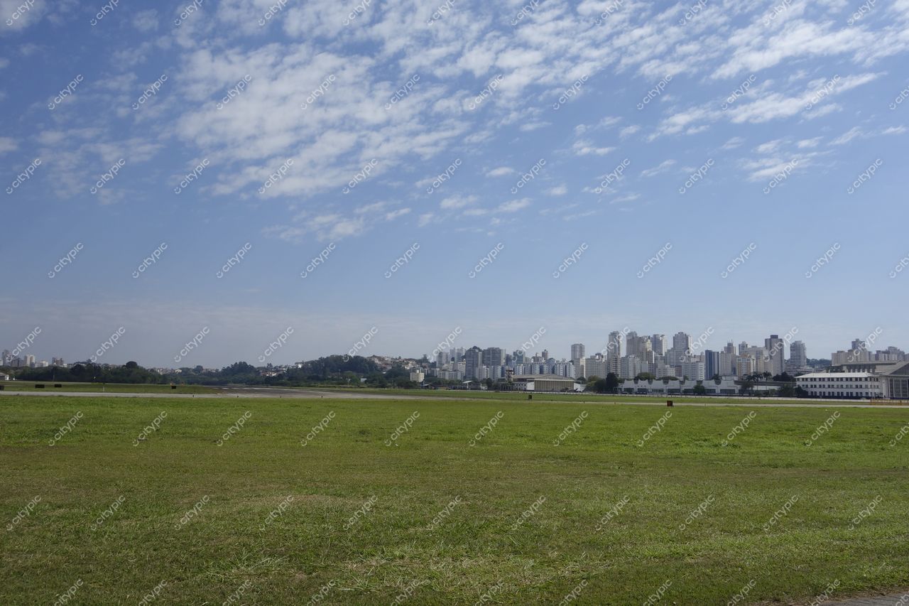 São Paulo, São Paulo, vista panorâmica com gramado verde em primeiro plano e prédios modernos ao fundo sob céu nublado