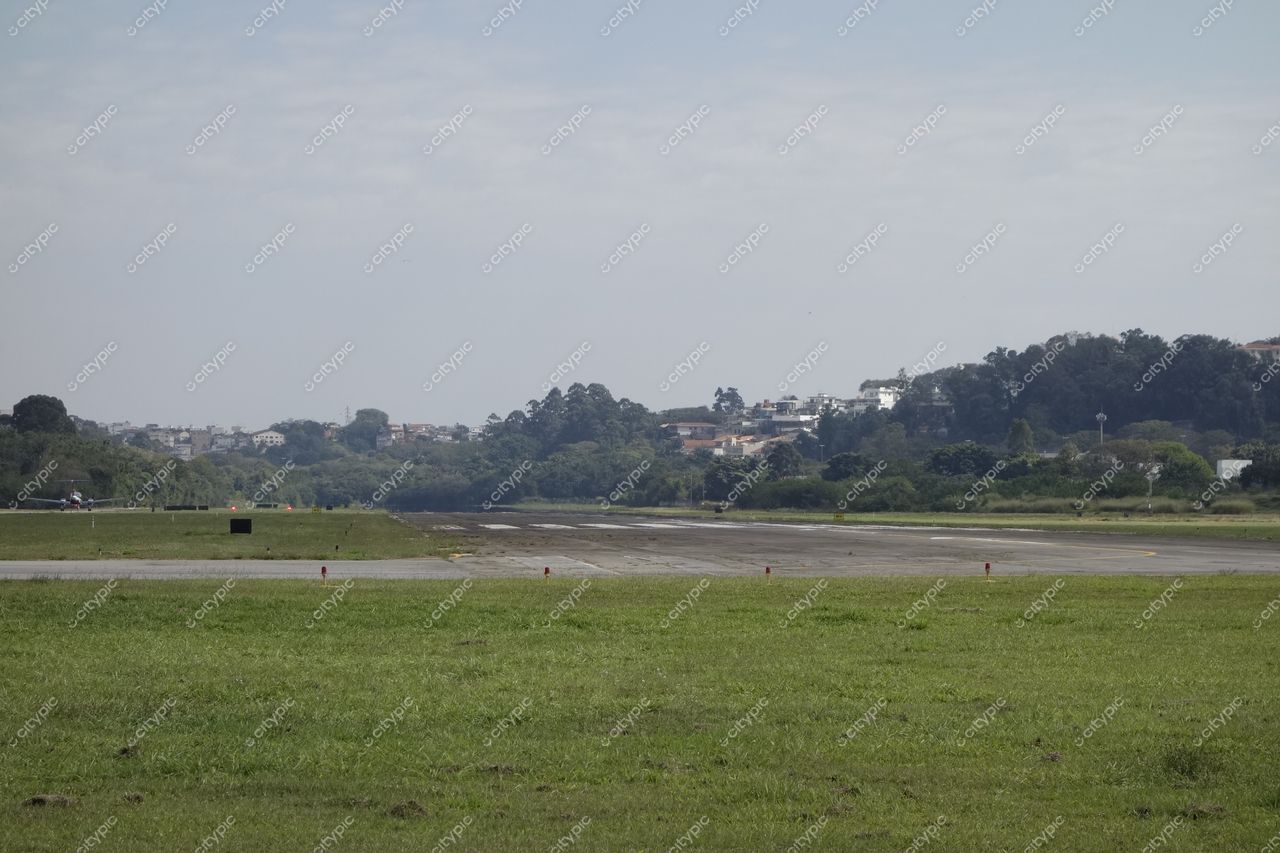 São Paulo, São Paulo, pista de pouso em aeroporto com vegetação e área urbana ao fundo em dia claro