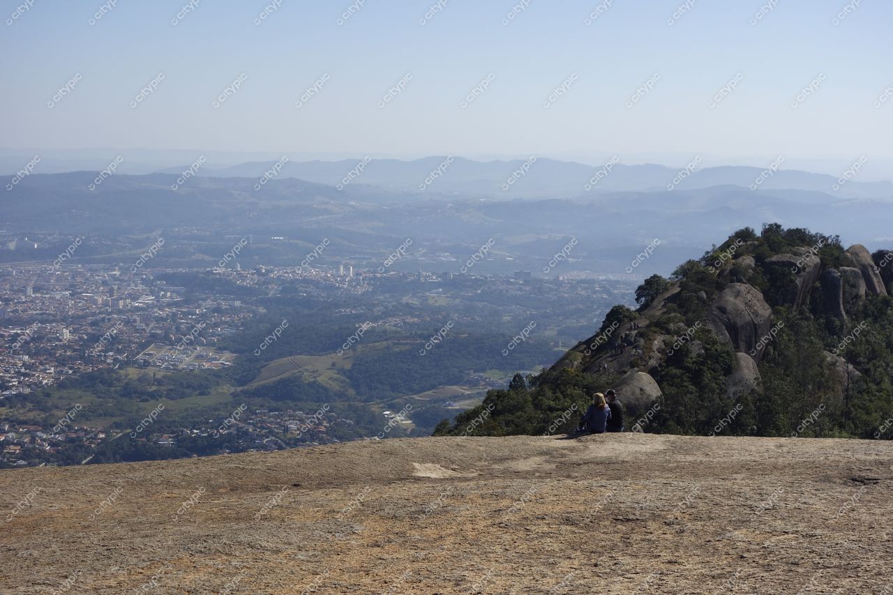Atibaia, São Paulo vista panorâmica com montanhas ao fundo e pessoas sentadas em pedra clara sob céu azul