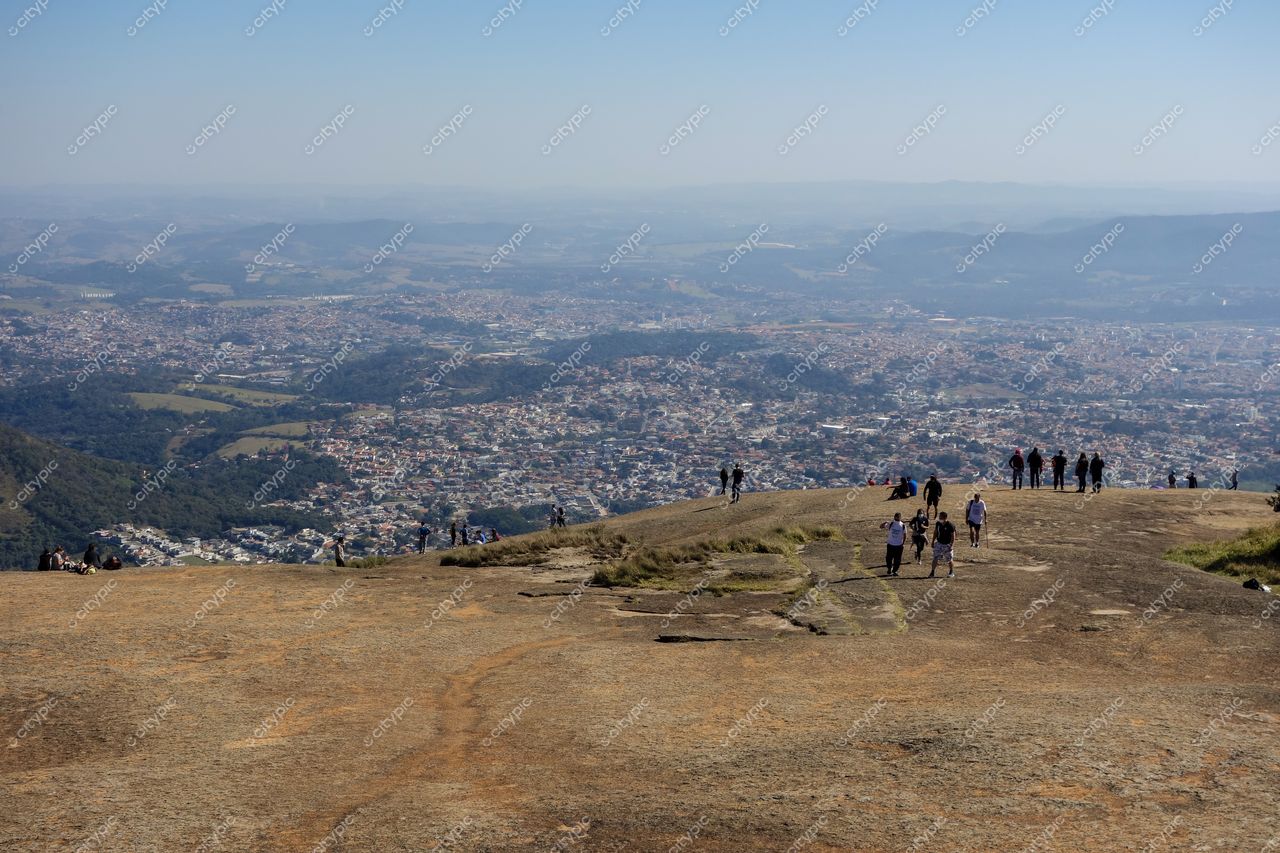 Atibaia, São Paulo vista do alto com montanhas ao fundo e pessoas caminhando em superfície rochosa iluminada pelo dia
