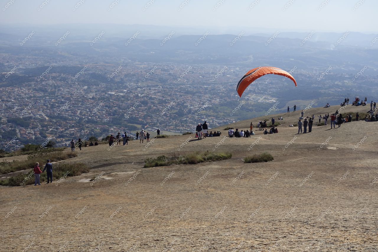 Atibaia, São Paulo com paragliding laranja sobre colinas e vegetação em dia ensolarado e pessoas ao ar livre