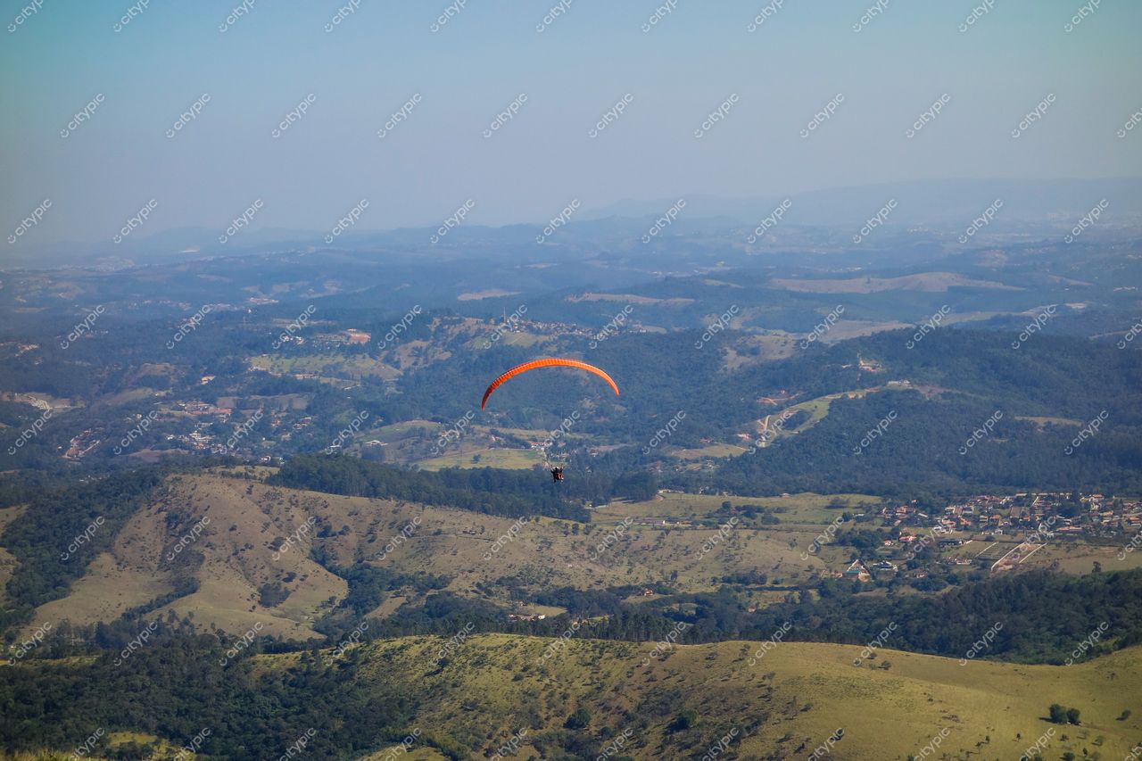Atibaia, São Paulo, parapente laranja sobre colinas verdes em dia claro com áreas urbanas ao fundo