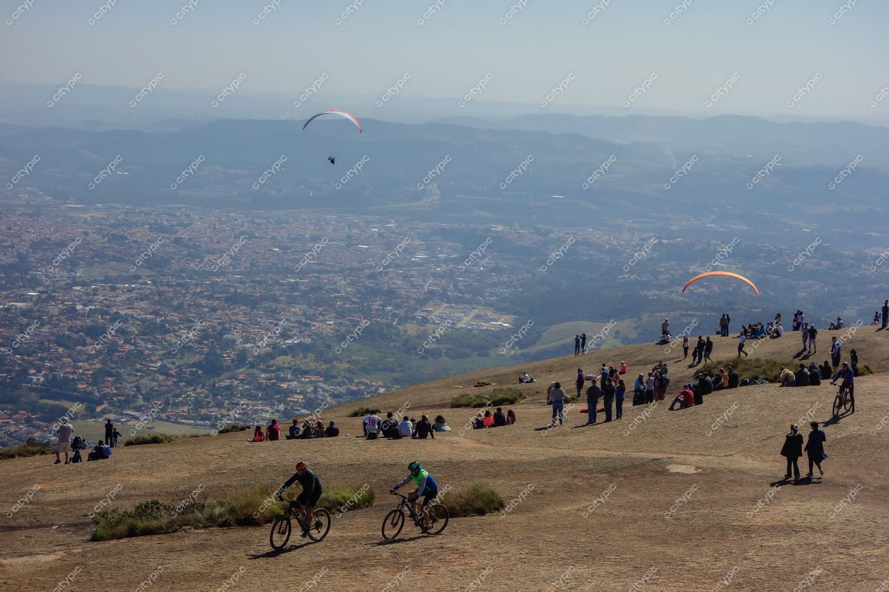 Atibaia, São Paulo com paragliders coloridos no céu e ciclistas em superfície rochosa em dia ensolarado
