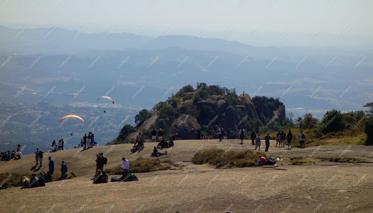 Atibaia, São Paulo, pessoas no topo da Pedra Grande em dia ensolarado com parapentes e colinas ao fundo