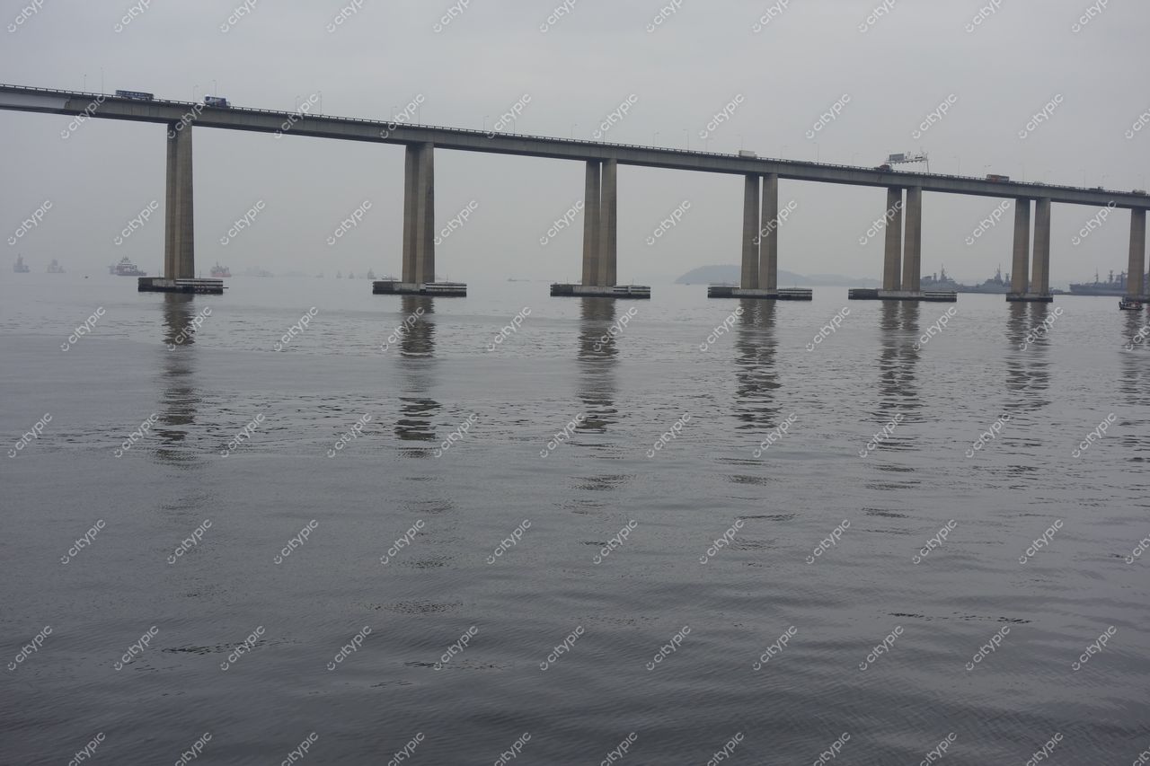 Rio de Janeiro, Rio de Janeiro, ponte suspensa sobre águas calmas com céu nublado e pequenas embarcações ao fundo