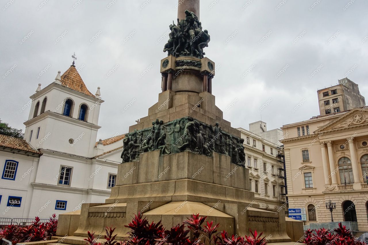 São Paulo, São Paulo, monumento com esculturas em bronze e base de pedra em ambiente urbano nublado com vegetação colorida