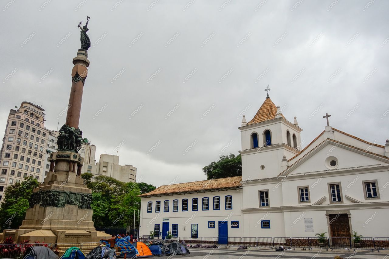 São Paulo, São Paulo, praça com monumento imponente e igreja colonial em dia nublado com barracas de camping