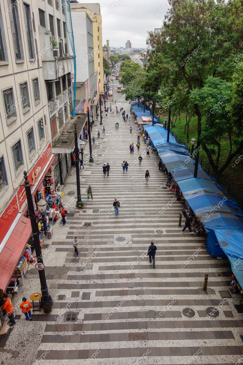 São Paulo, São Paulo, vista elevada de rua com calçadas largas, vendedores sob lona azul e céu nublado
