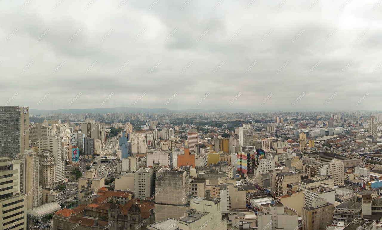 São Paulo, São Paulo, vista panorâmica sob céu nublado com edifícios variados e ruas movimentadas e vegetação ao fundo