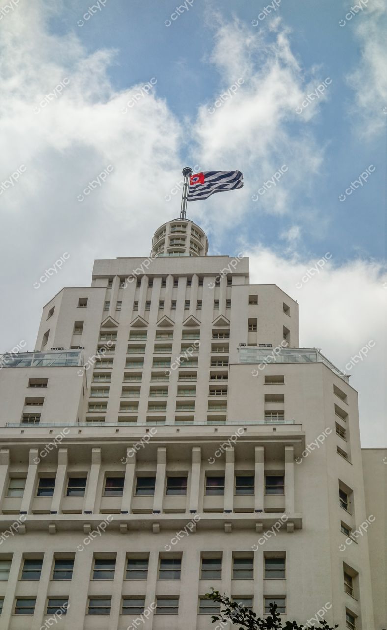 São Paulo, São Paulo, edifício alto com arquitetura moderna e bandeira visível sob céu azul nublado em ambiente urbano