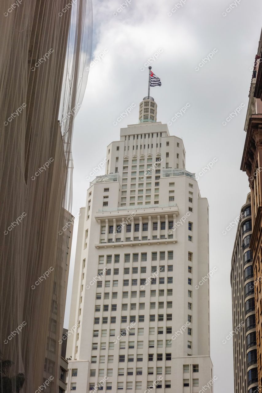 São Paulo, São Paulo, edifício art déco branco com torre e bandeira em dia nublado entre vegetação urbana