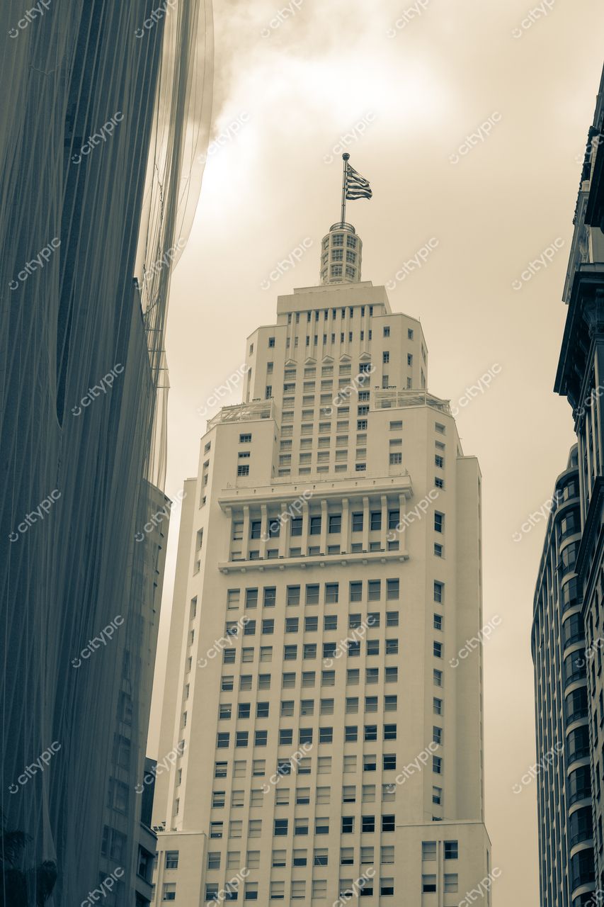 São Paulo, São Paulo, edifício clássico com torre e bandeira do Brasil em meio a arquitetura moderna e céu nublado