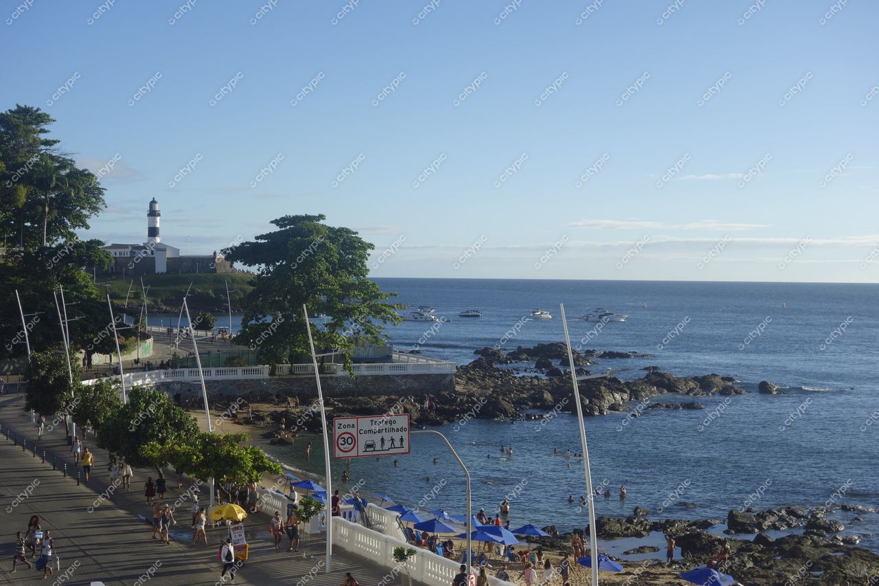 Farol da Barra em Salvador com luz do final da tarde, rochas na orla e barcos ancorados na costa