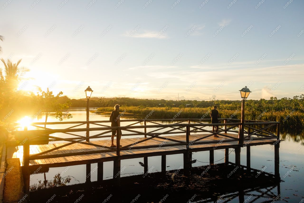 Mata de São João, Bahia, pier de madeira ao pôr do sol com vegetação iluminada e pessoas contemplando a paisagem
