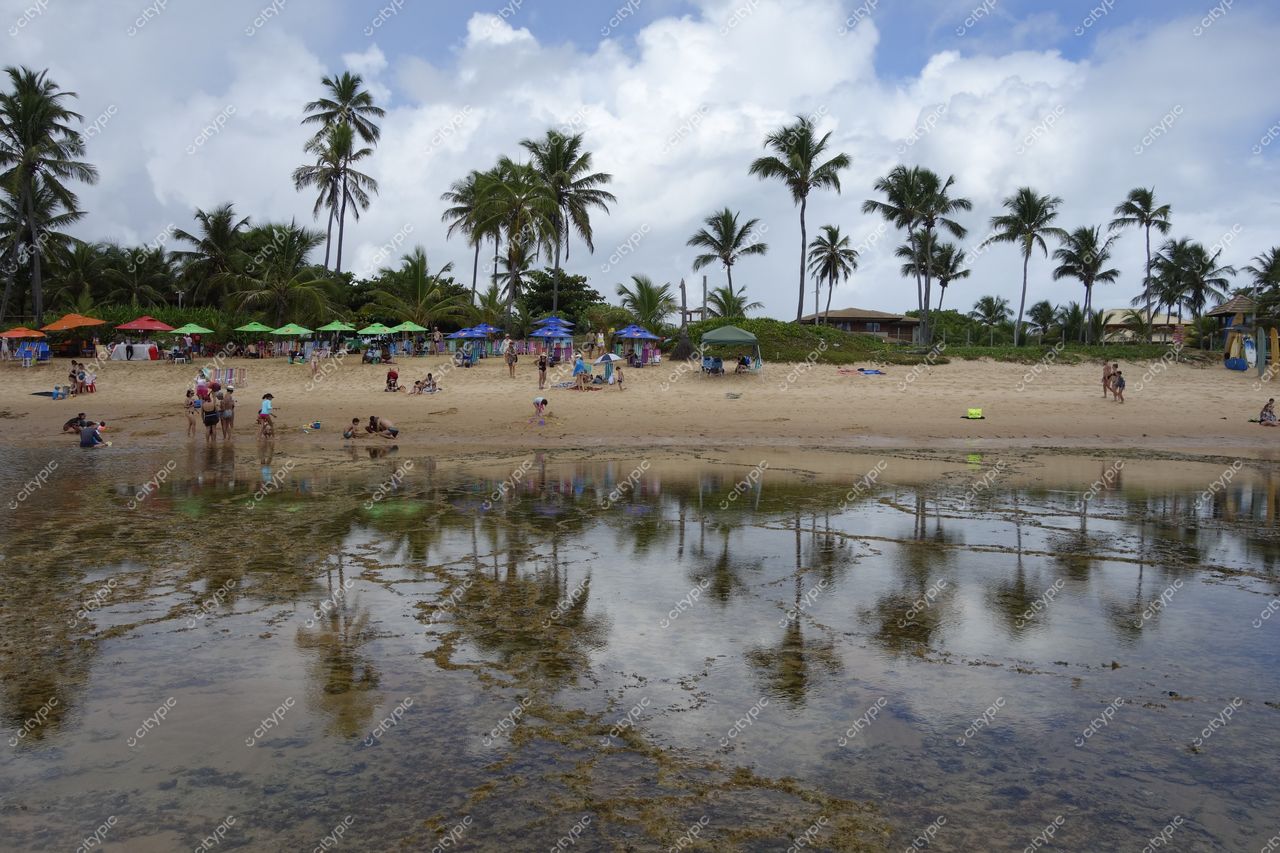Mata de São João, Bahia, dia nublado com pessoas na praia e guarda-sóis coloridos em ambiente tranquilo