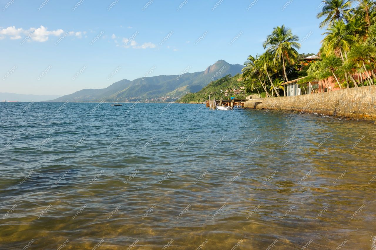 Ilhabela, São Paulo com águas calmas refletindo luz do sol e montanhas verdes sob céu parcialmente nublado