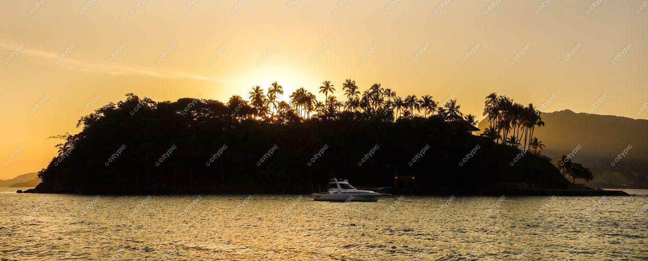 Ilhabela, São Paulo ao amanhecer com palmeiras, barco de passeio e montanhas ao fundo em luz suave