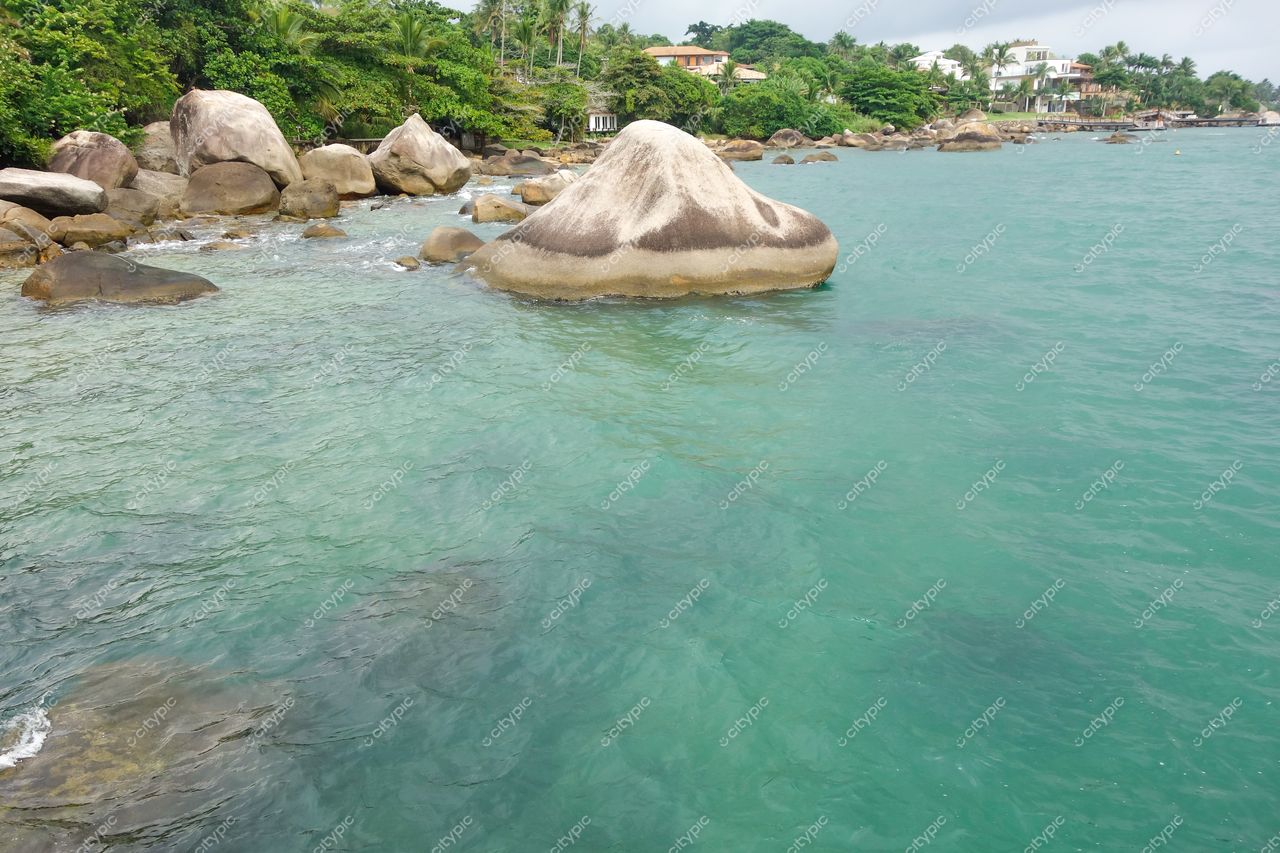 Ilhabela, São Paulo vista da costa com grandes rochas, mar azul e verde, construções residenciais e vegetação tropical