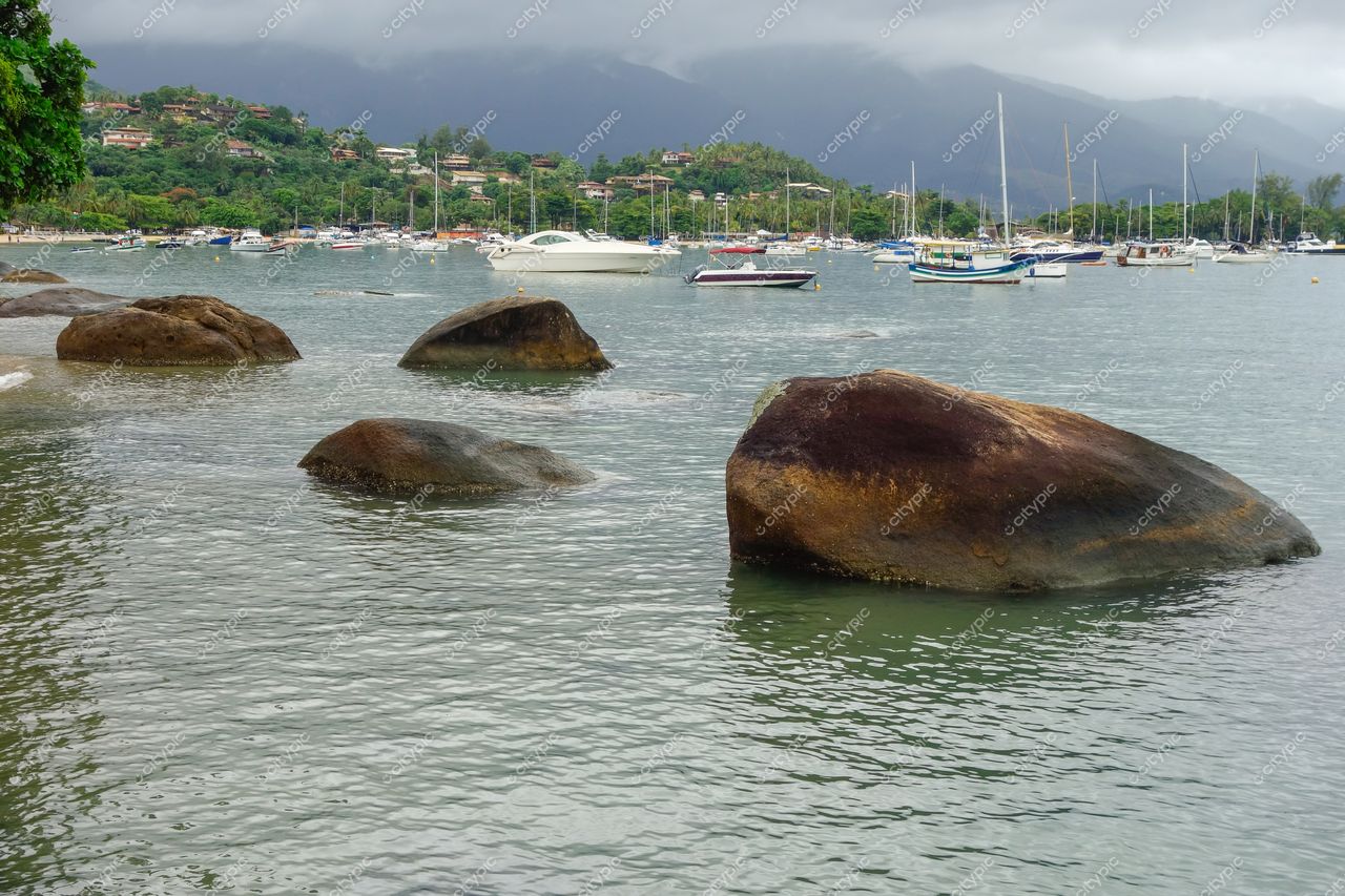 Ilhabela, São Paulo vista serena do mar com rochas, embarcações atracadas e vegetação exuberante ao fundo