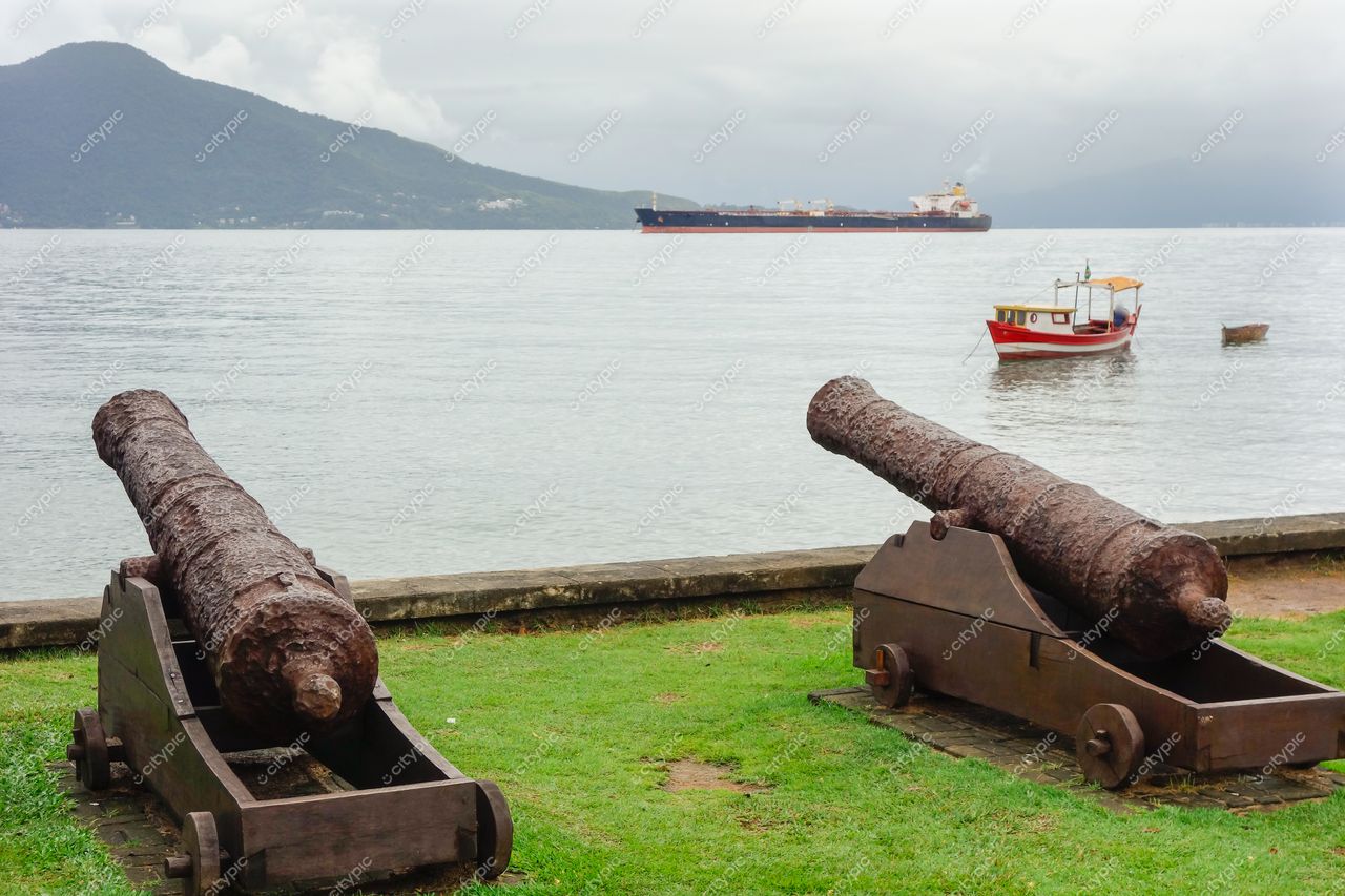 Ilhabela, São Paulo com canhões em primeiro plano e navio cargueiro ao fundo em dia nublado