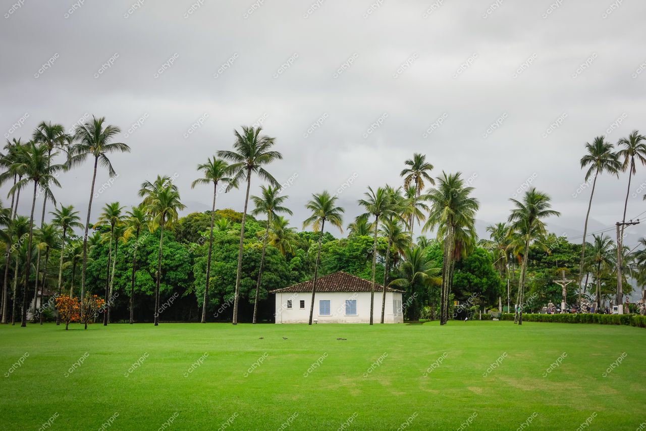 Ilhabela, São Paulo, casa branca com telhado de cerâmica cercada por palmeiras sob céu nublado e gramado verde