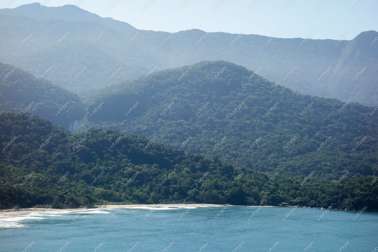 Ilhabela, São Paulo, montanhas verdes com cachoeira ao fundo e costa com ondas suaves em dia ensolarado
