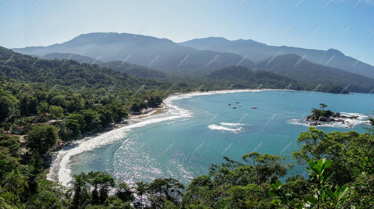 Ilhabela, São Paulo vista panorâmica da costa com águas azuis e vegetação densa sob céu ensolarado e montanhas ao fundo