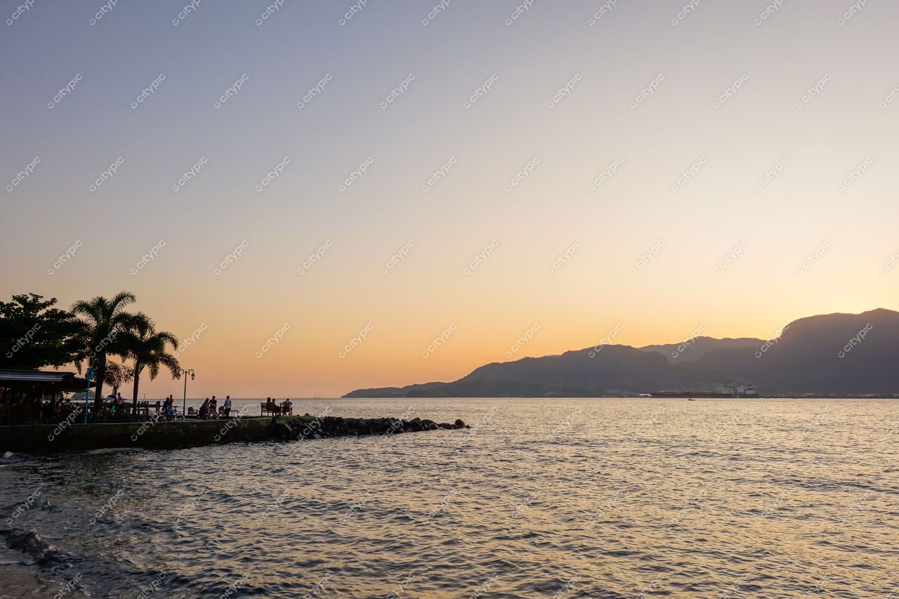 Ilhabela, São Paulo captura pôr do sol com vegetação tropical, pessoas na praia e montanhas ao fundo