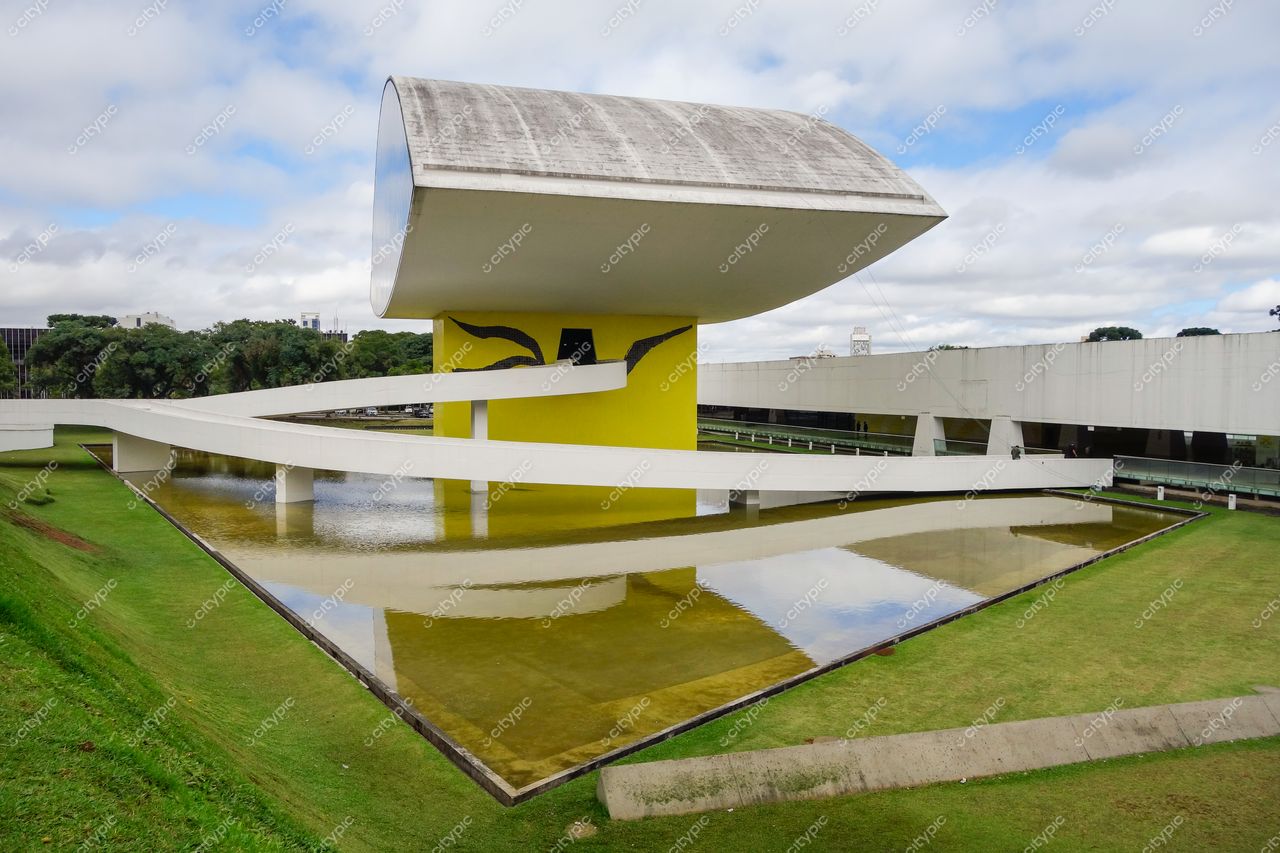 Museu Oscar Niemeyer em Curitiba com céu nublado e espelho d’água refletindo a arquitetura contemporânea e paisagem urbana