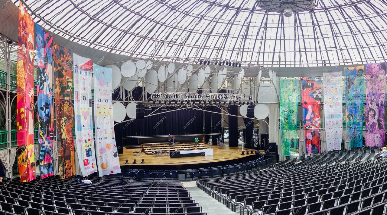 Ópera de Arame em Curitiba com interior iluminado, palco preparado e painéis decorativos coloridos nas laterais