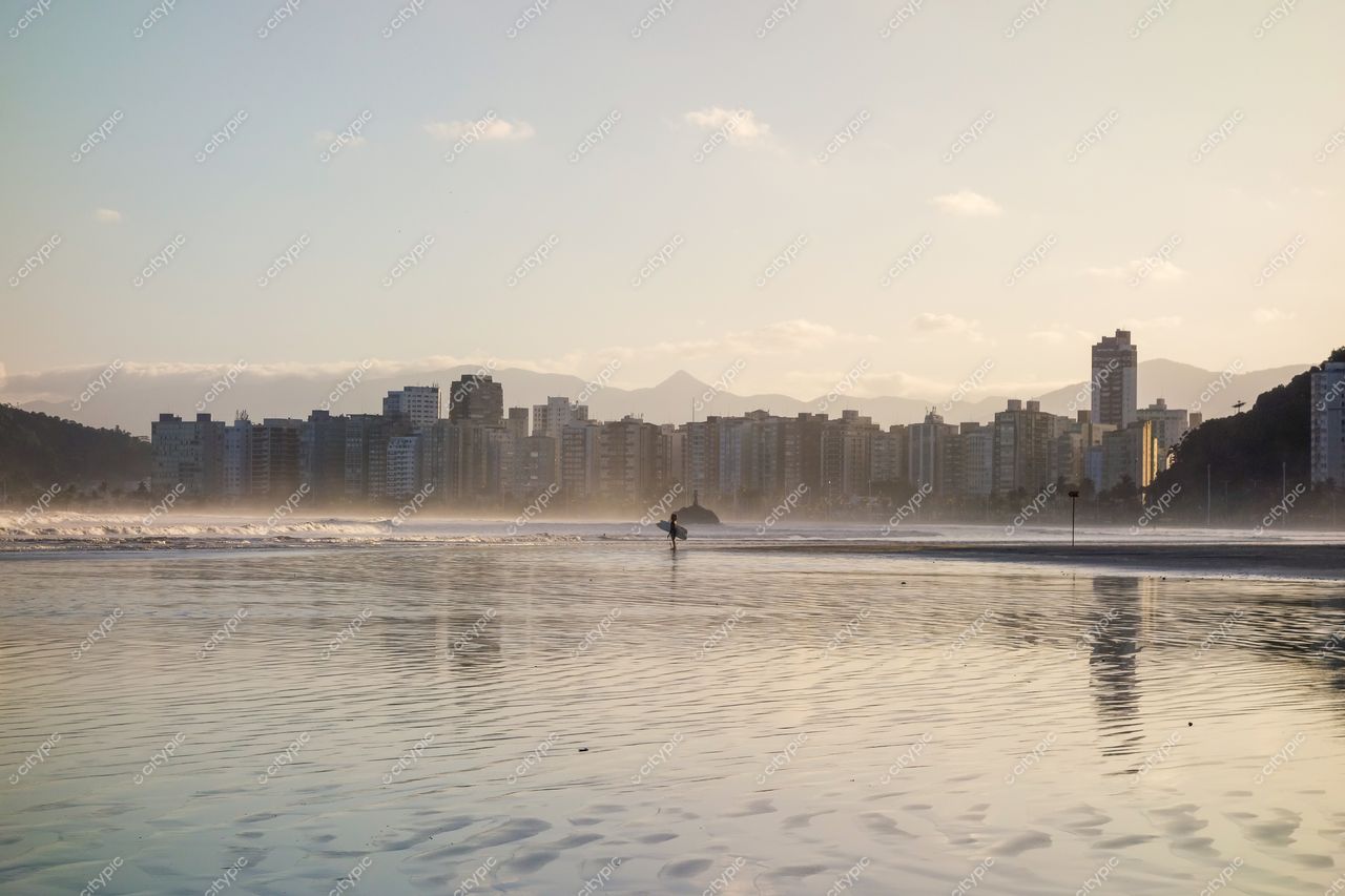 Santos, São Paulo, amanhecer com arranha-céus refletindo luz suave e surfista em mar calmo com nevoeiro