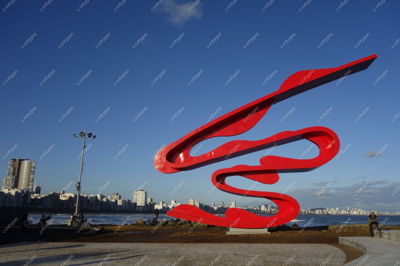 Monumento Tomie Ohtake em Santos com céu azul e pessoas interagindo na orla urbana à beira-mar