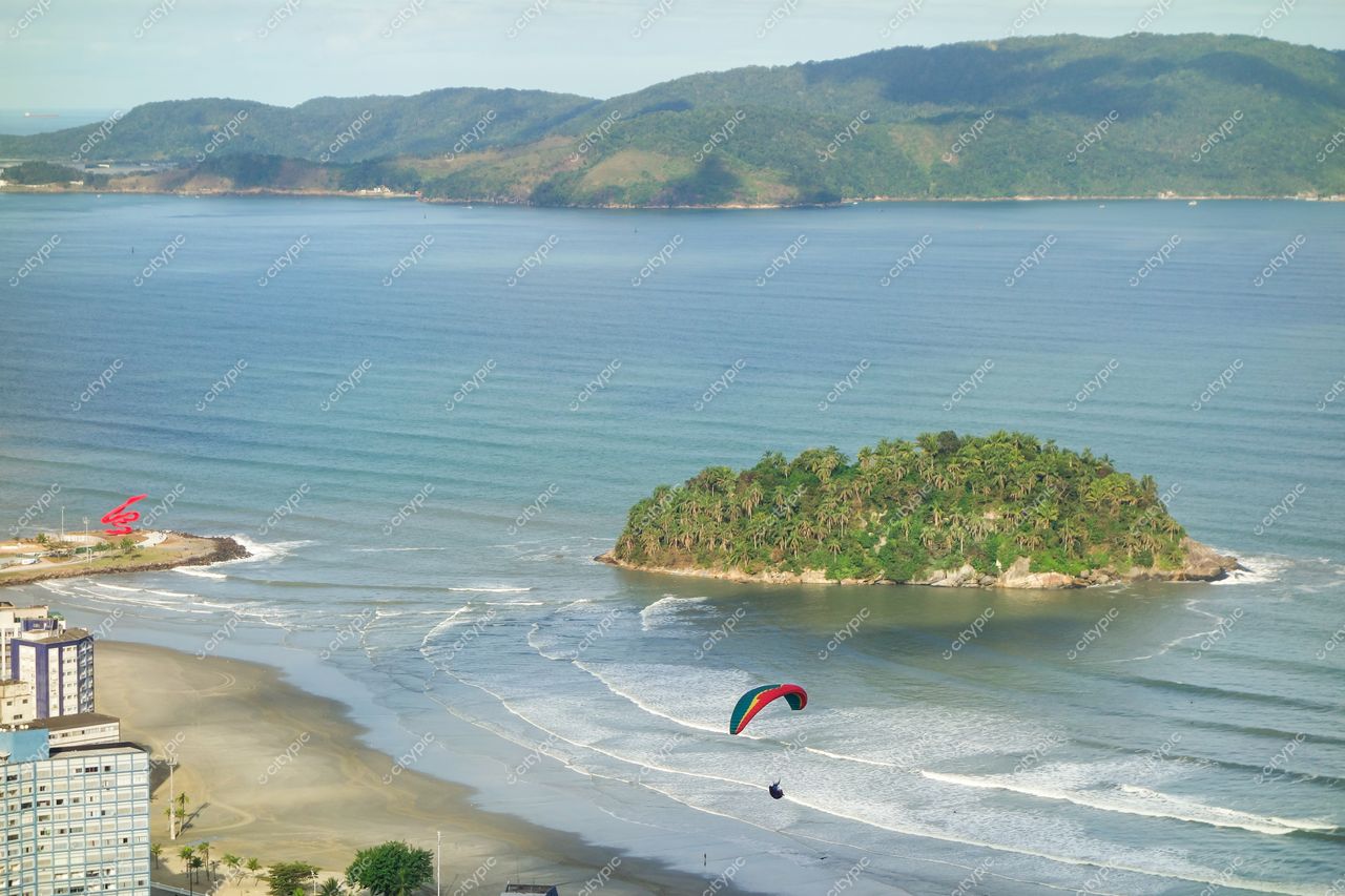 Santos, São Paulo, vista da costa com mar calmo, ilha verde ao fundo e parapente sobre a praia