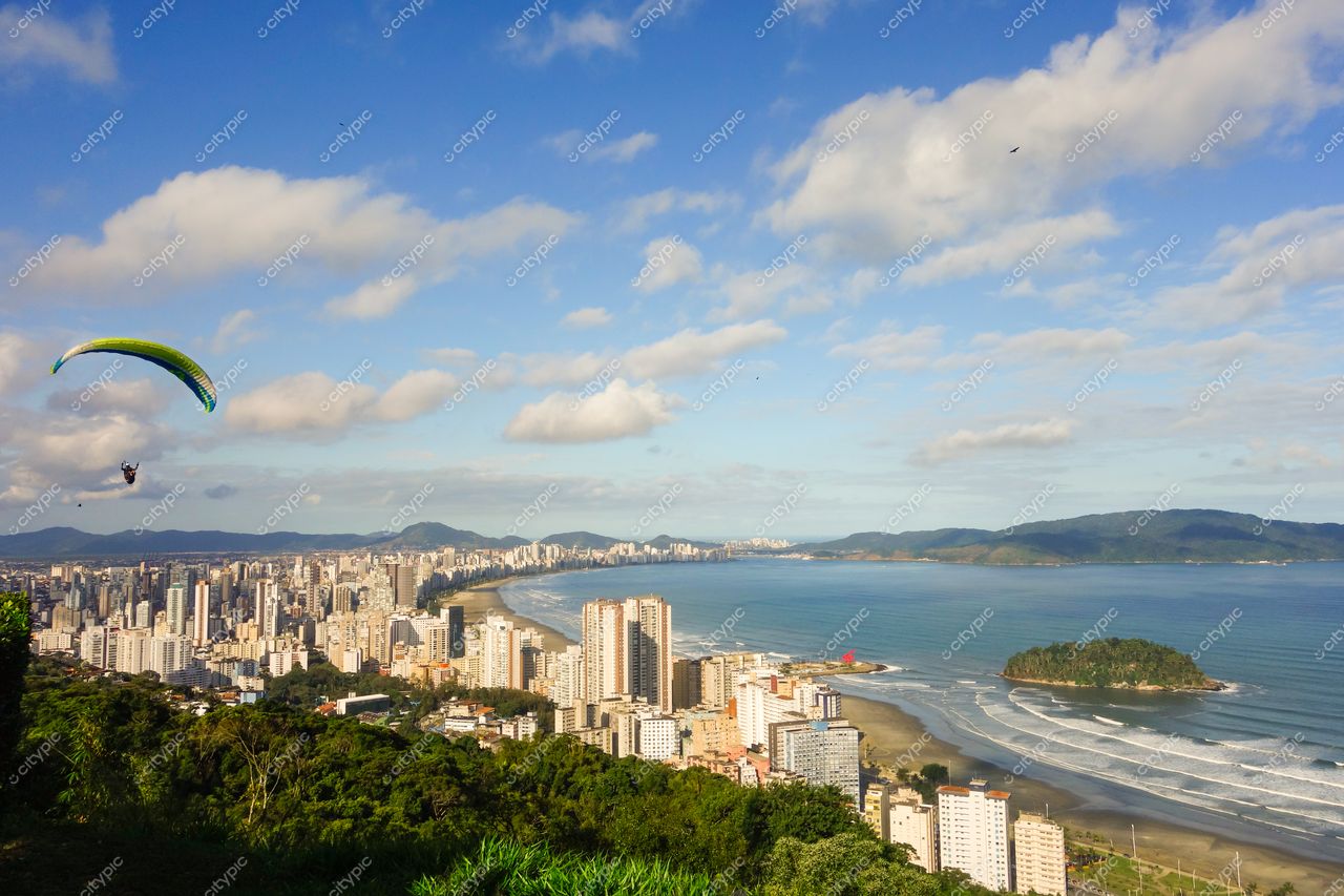 Santos, São Paulo, vista panorâmica em dia ensolarado com parapente sobre a orla e montanhas ao fundo
