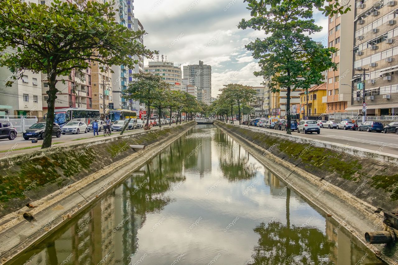 Santos, São Paulo, canal urbano com água calma refletindo céu nublado e tráfego nas ruas adjacentes