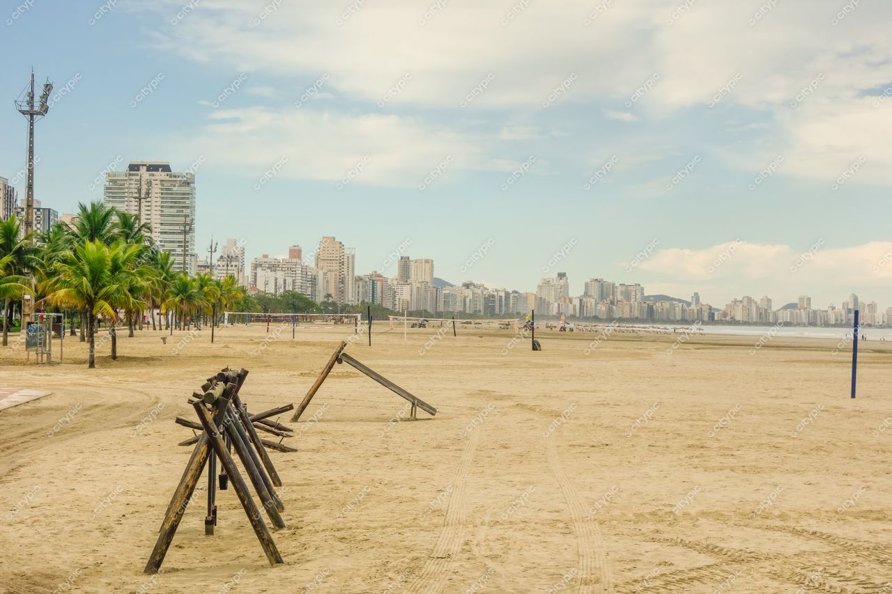 Santos, São Paulo, praia com estruturas de madeira e palmeiras em dia claro, prédios modernos ao fundo