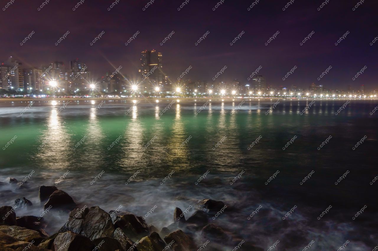 Santos, São Paulo, orla noturna com mar verde esmeralda e reflexos das luzes urbanas em edifícios altos