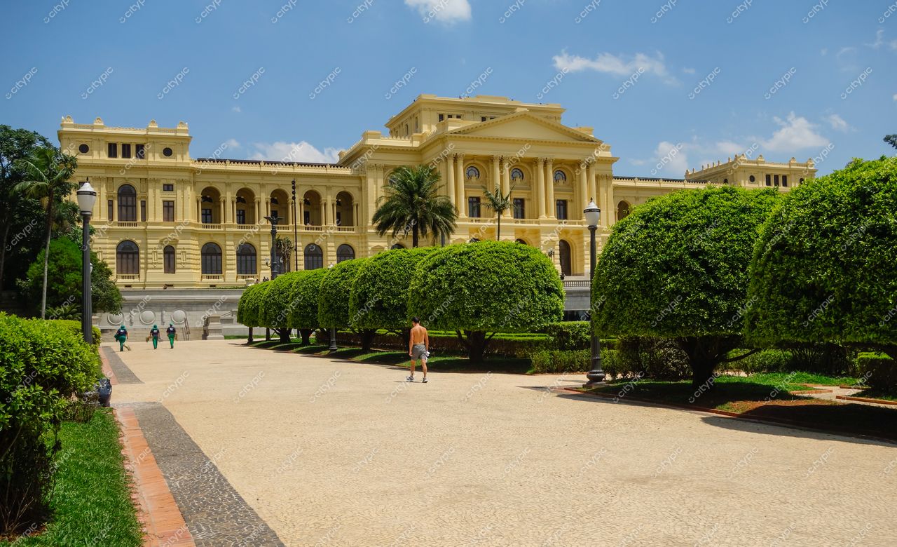 São Paulo, São Paulo, fachada de edifício amarelo com jardim e palmeiras em dia ensolarado e calçada tranquila