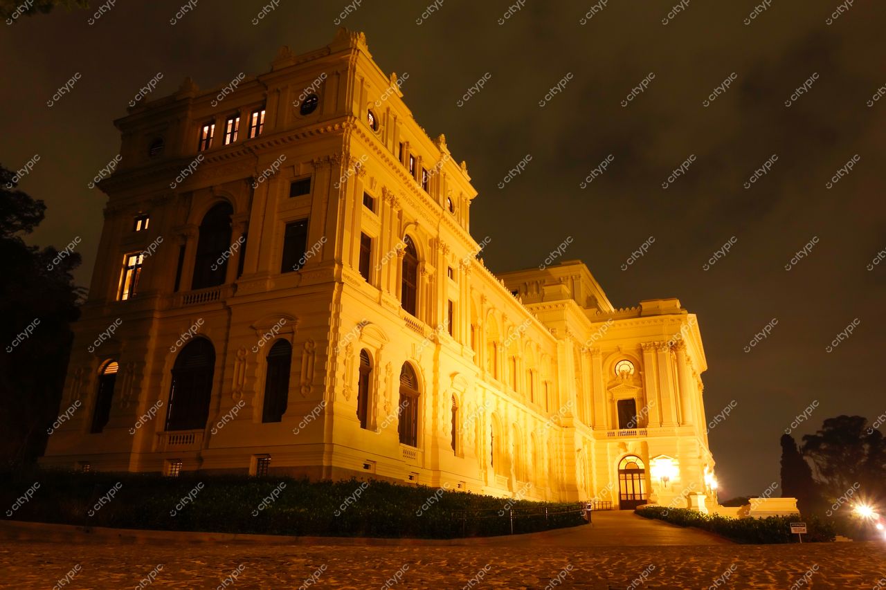 São Paulo, São Paulo, edifício histórico neoclássico iluminado à noite com vegetação baixa e céu nublado