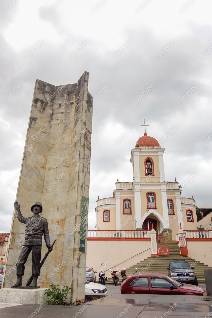Centro Histórico de São João del Rei em dia nublado com monumento de soldado e igreja colonial ao fundo