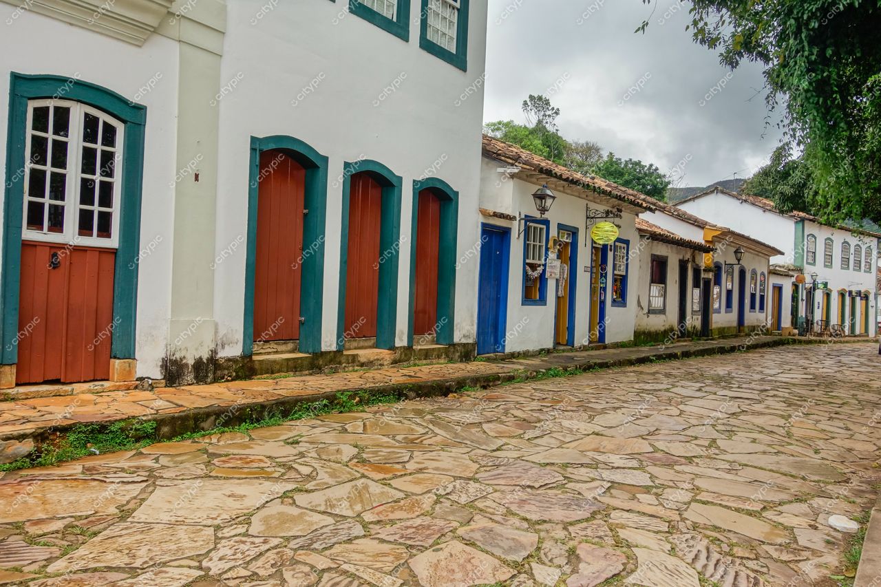 Tiradentes, Minas Gerais, rua colonial com casas brancas e portas azuis e vermelhas sob luz difusa em dia nublado