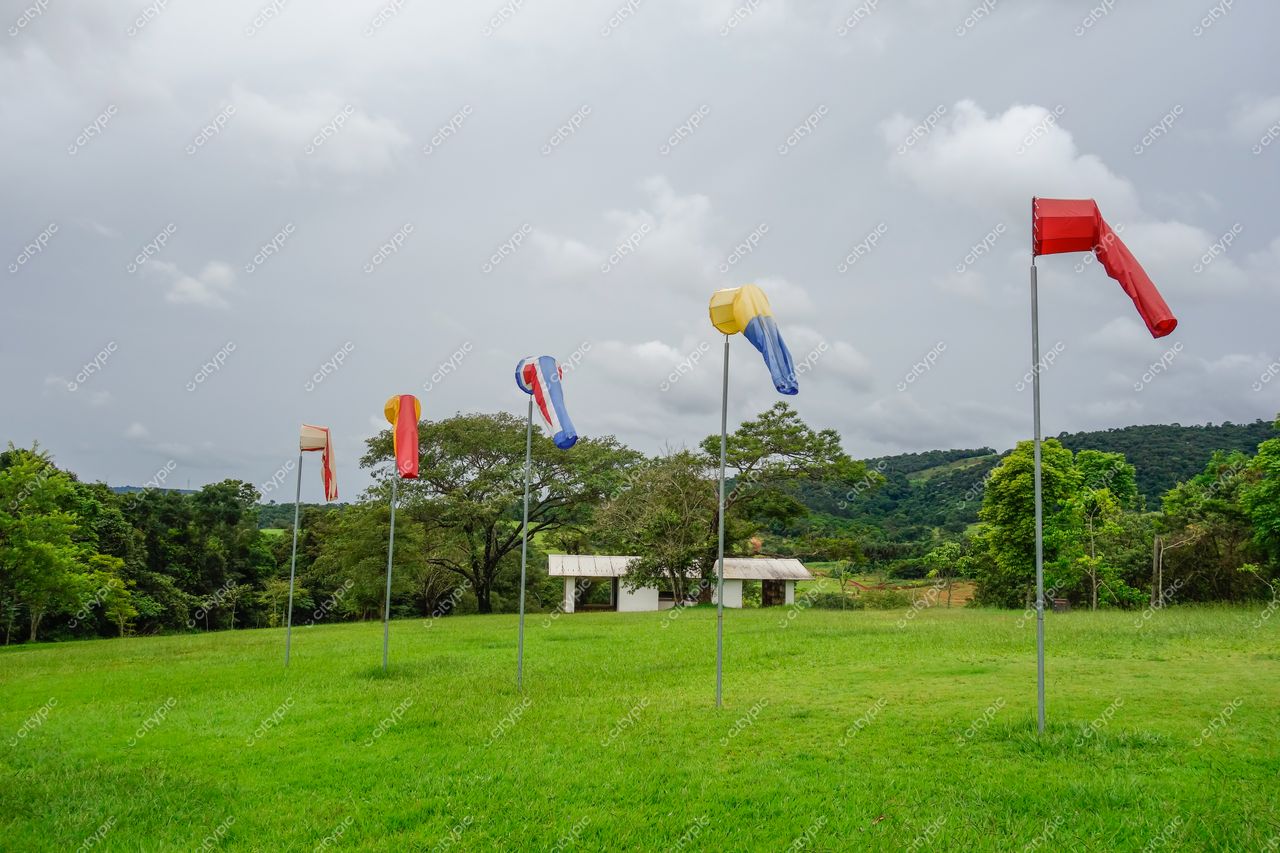 Brumadinho, Minas Gerais campo verdejante com bandeiras coloridas em postes sob céu nublado e construção simples ao fundo