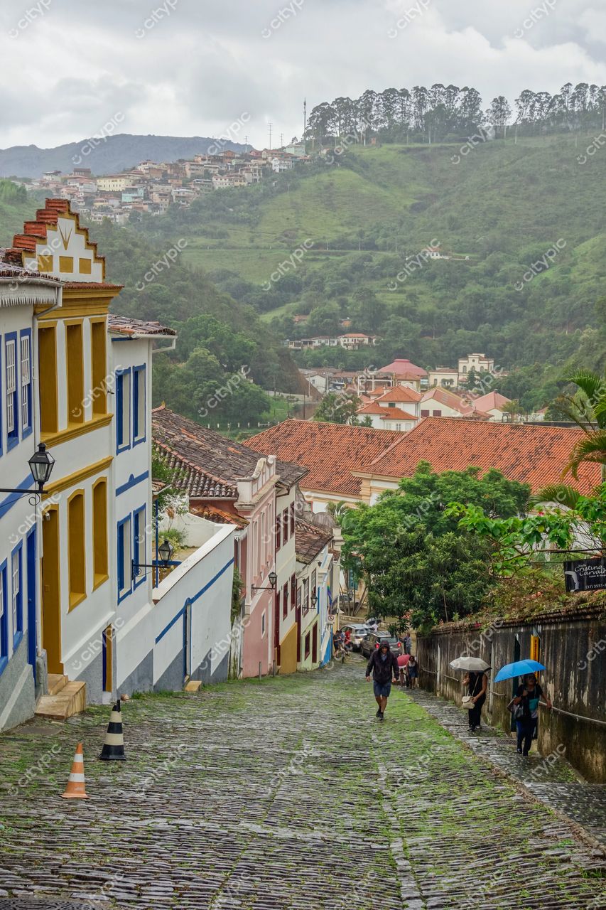 Ouro Preto, Minas Gerais, rua descendente com calçamento de pedras e casas coloniais azuis e amarelas sob céu nublado