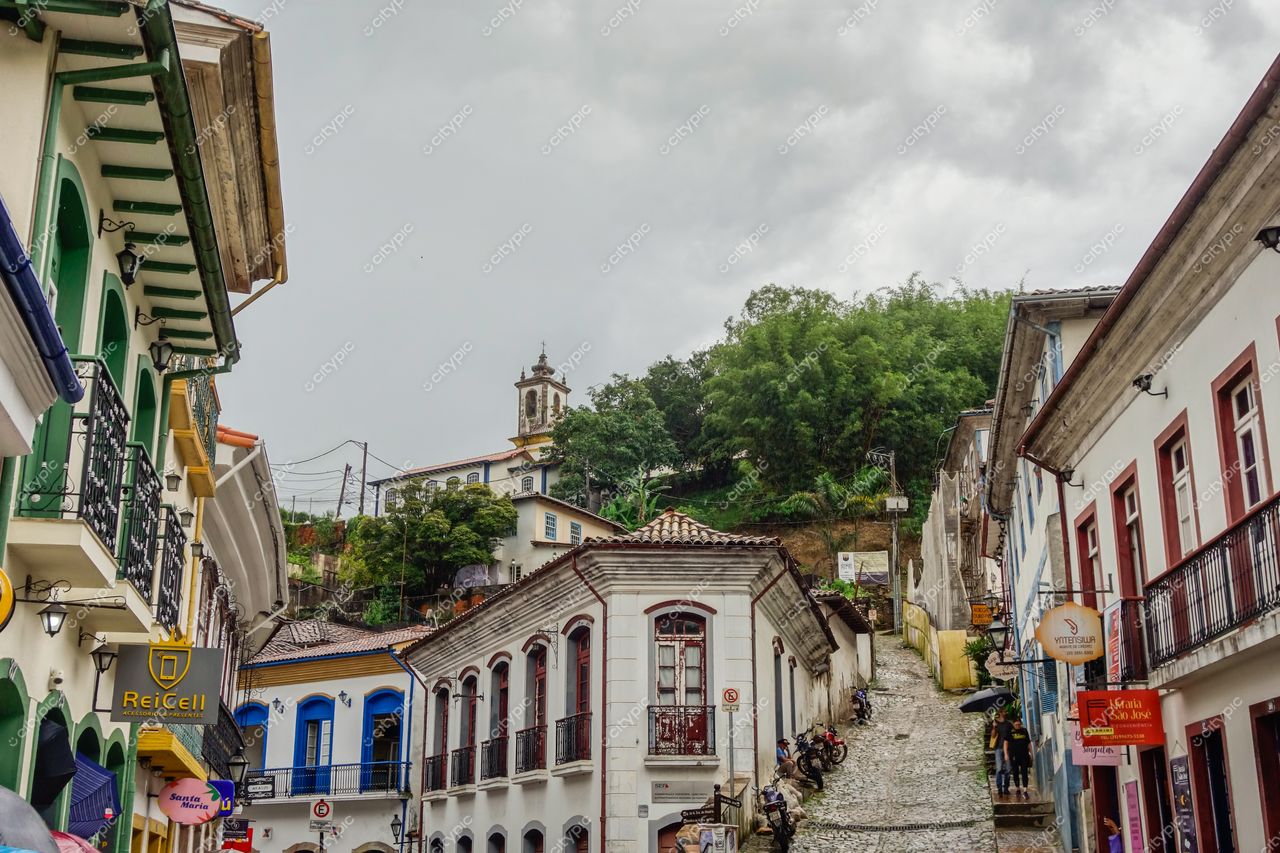 Ouro Preto, Minas Gerais, rua charmosa com arquitetura colonial, casas coloridas e vegetação densa sob céu nublado