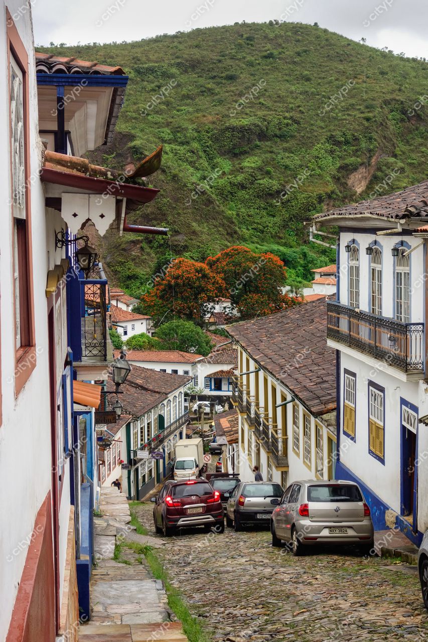 Ouro Preto, Minas Gerais, rua íngreme com casas coloniais coloridas e colina verdejante sob céu nublado